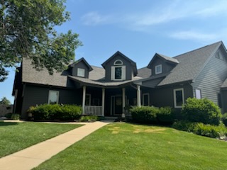 Two-story tan home with dark shingle roofing and an attached two-car garage.